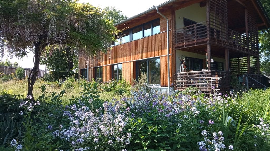 Ein blühender Garten. Im Hintergrund ein Wohnhaus mit Holzfassade.