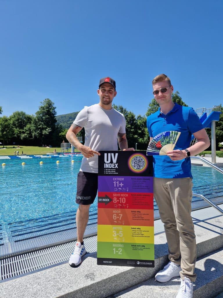 Zwei Personen im Freibad halten eine bunte Tafel.