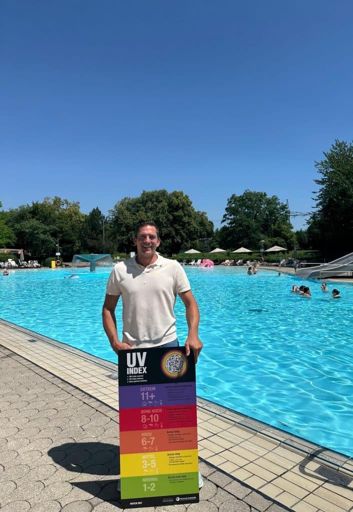 Eine Person im Freibad hält eine bunte Tafel.