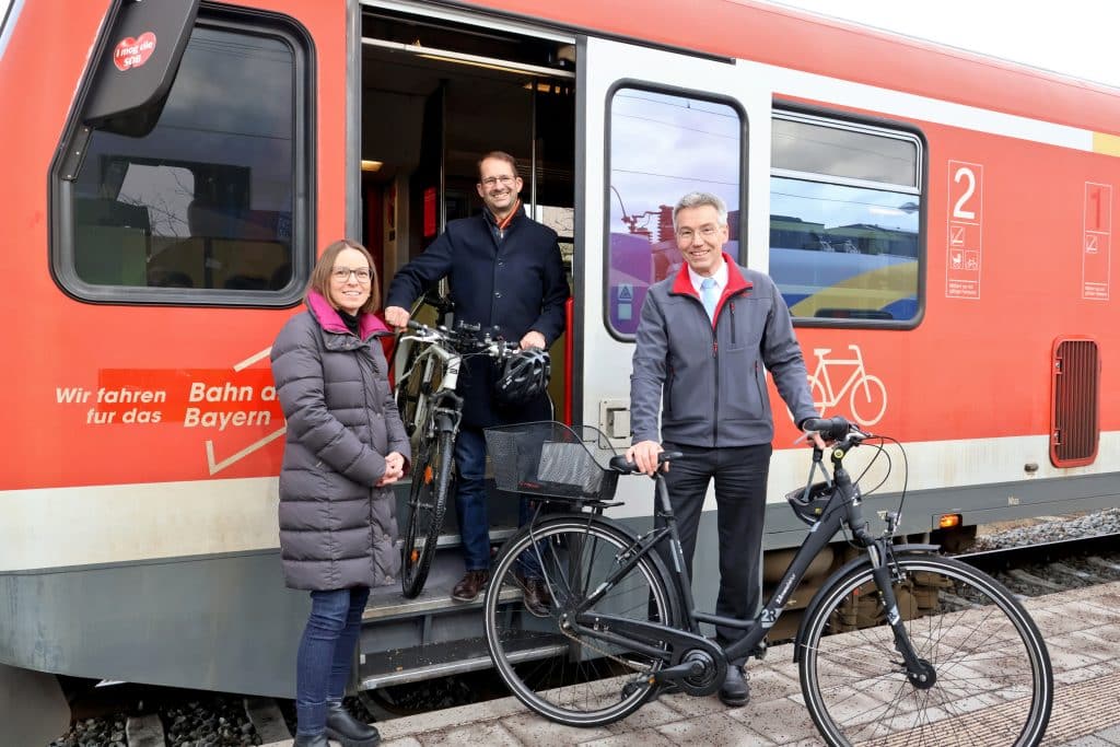 Drei Personen mit Fahrrädern vor einem roten Zug.