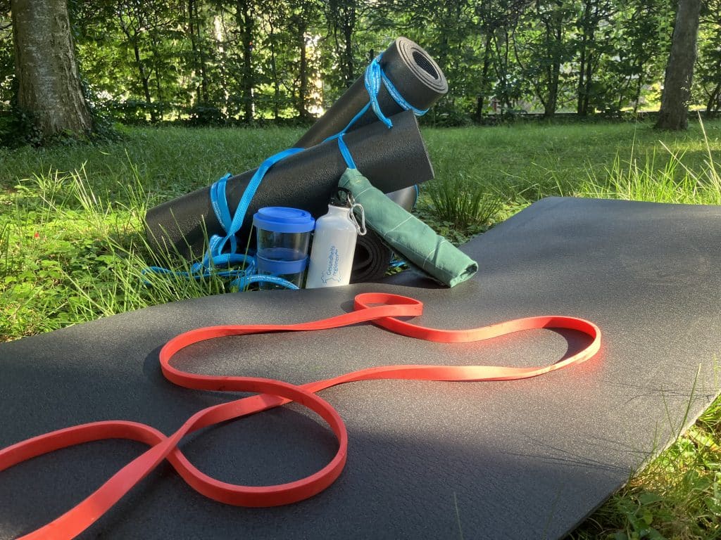Verschiedenes Sportzubehör wie eine Trinkflasche und Yogamatten im Freien.