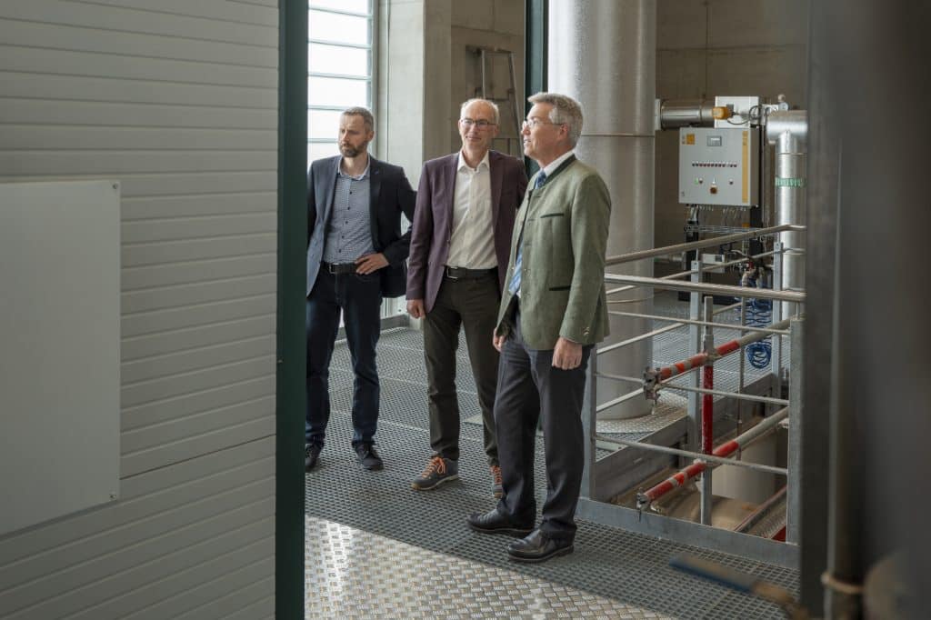 Drei Personen stehen in einem Industrieraum.